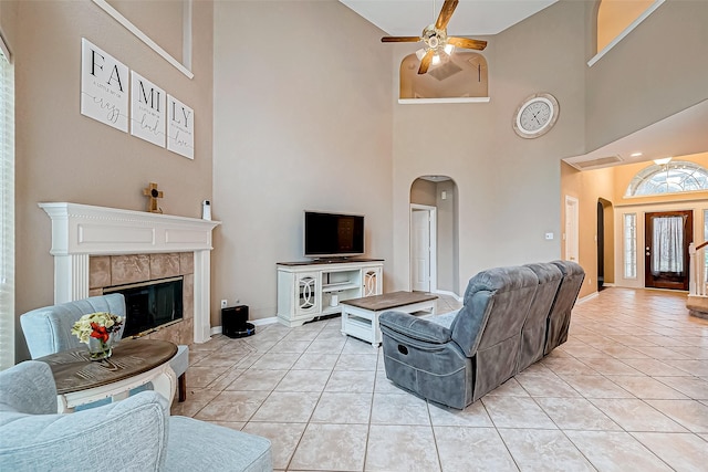 tiled living room featuring ceiling fan, a towering ceiling, and a tile fireplace