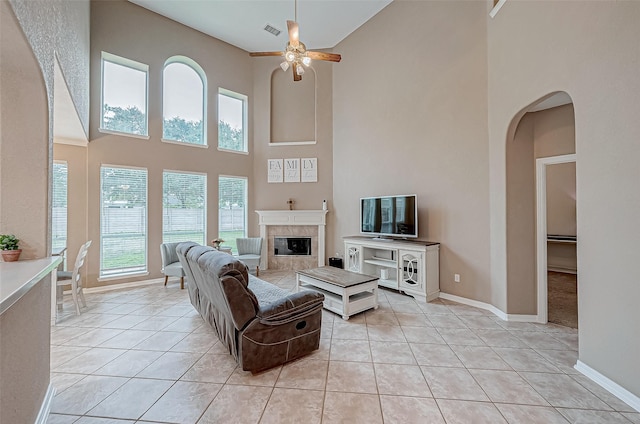 living room with a fireplace, ceiling fan, light tile patterned flooring, and a towering ceiling