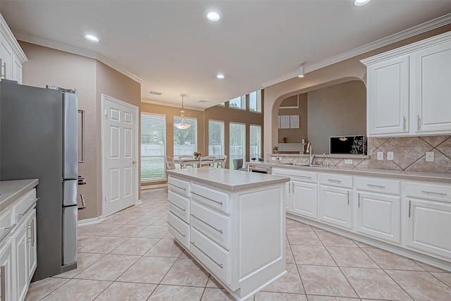 kitchen with white cabinetry, hanging light fixtures, crown molding, and stainless steel refrigerator