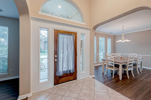 tiled entryway with crown molding and an inviting chandelier