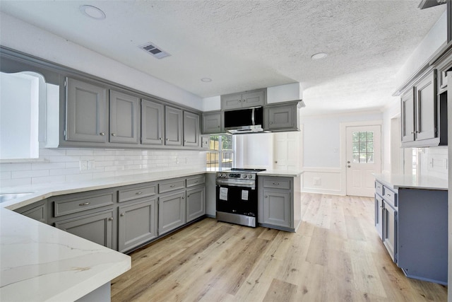 kitchen featuring gray cabinetry, decorative backsplash, stainless steel stove, light hardwood / wood-style flooring, and light stone counters