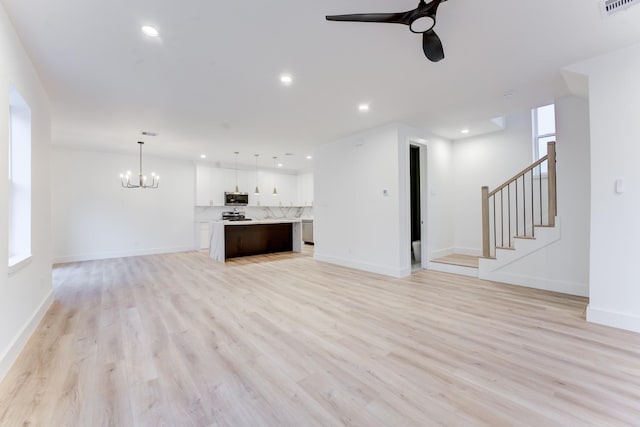 unfurnished living room featuring a wealth of natural light, ceiling fan with notable chandelier, and light hardwood / wood-style floors