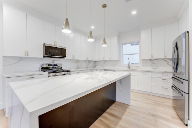 kitchen with sink, appliances with stainless steel finishes, white cabinetry, a center island, and decorative light fixtures