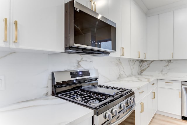 kitchen featuring stainless steel appliances, white cabinets, and light stone counters