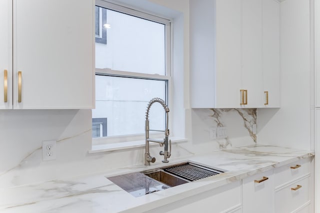 kitchen featuring light stone countertops, sink, white cabinets, and backsplash