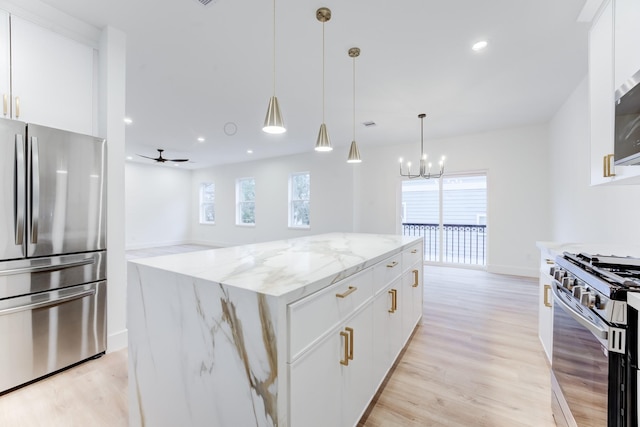 kitchen with a kitchen island, ceiling fan with notable chandelier, white cabinets, light stone counters, and stainless steel appliances