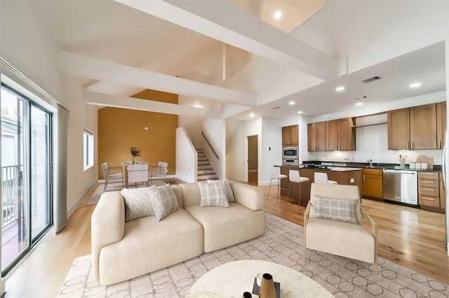 living room featuring high vaulted ceiling, sink, and light hardwood / wood-style flooring