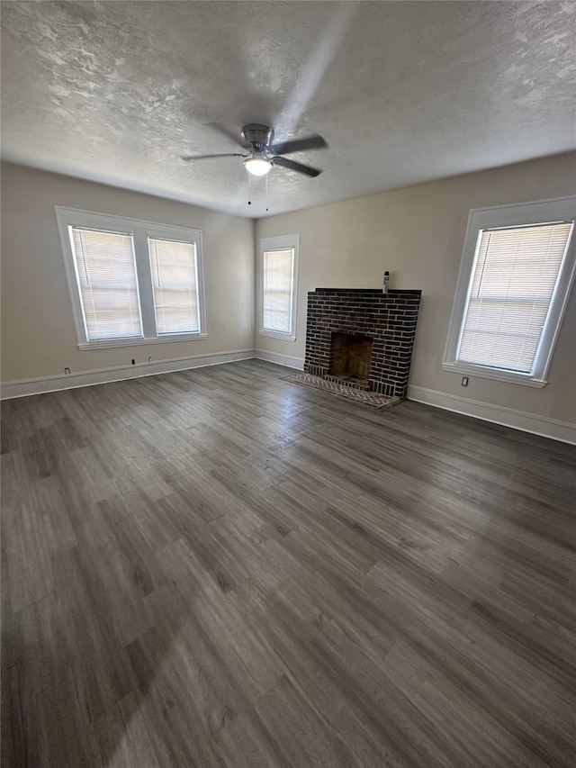 unfurnished living room featuring dark wood-type flooring, a brick fireplace, a textured ceiling, and ceiling fan