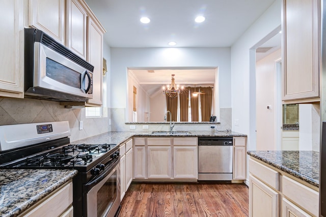 kitchen with a notable chandelier, stone counters, hardwood / wood-style floors, sink, and appliances with stainless steel finishes