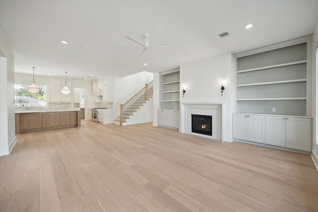 unfurnished living room featuring light hardwood / wood-style floors, built in features, and ceiling fan