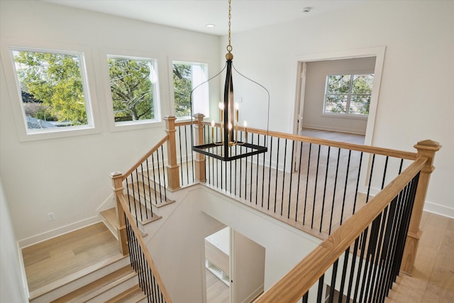 stairway featuring wood-type flooring, a wealth of natural light, and a chandelier