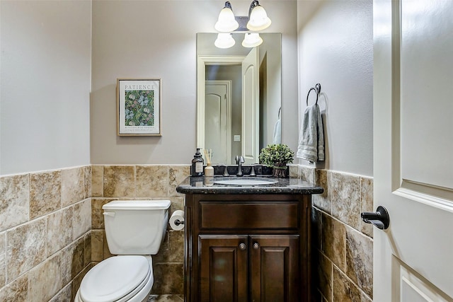 bathroom with toilet, an inviting chandelier, tile walls, and vanity