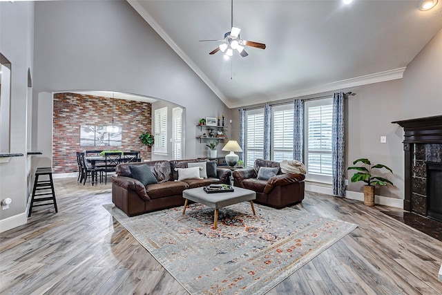 living room featuring ceiling fan, a fireplace, high vaulted ceiling, ornamental molding, and light hardwood / wood-style flooring