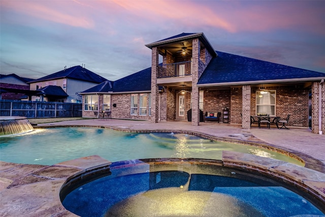 pool at dusk with ceiling fan, pool water feature, a patio area, and an in ground hot tub