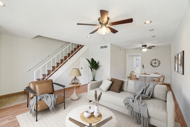 living room with ceiling fan, a textured ceiling, and light hardwood / wood-style flooring