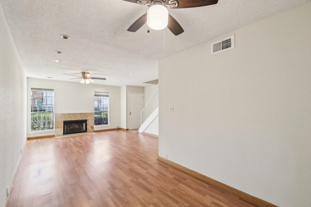 unfurnished living room featuring a tiled fireplace, a textured ceiling, and light hardwood / wood-style flooring