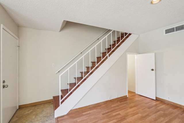 stairway with a textured ceiling and hardwood / wood-style floors