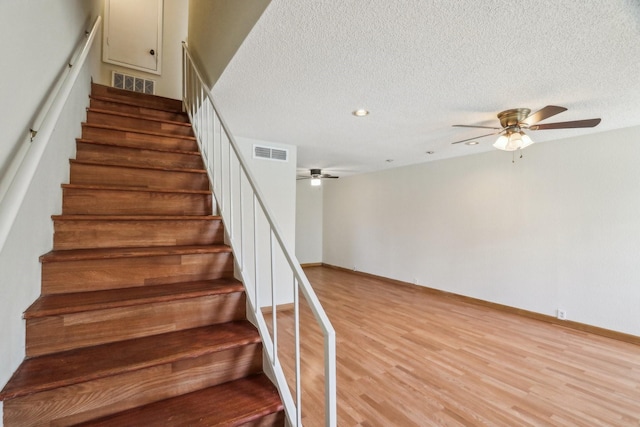 stairway featuring ceiling fan, wood-type flooring, and a textured ceiling