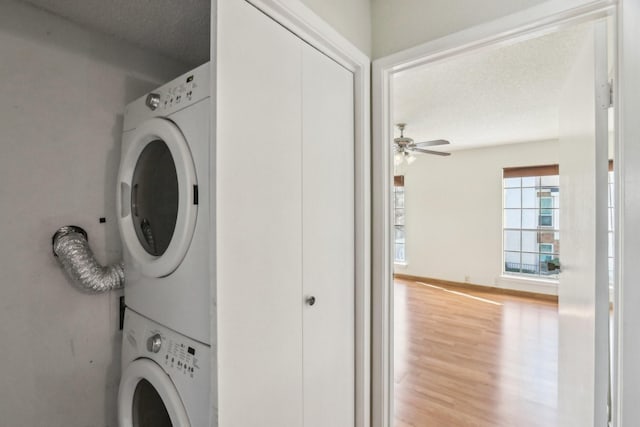 clothes washing area with ceiling fan, a textured ceiling, stacked washer / drying machine, and light wood-type flooring