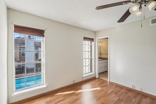 empty room featuring ceiling fan, plenty of natural light, wood-type flooring, and a textured ceiling