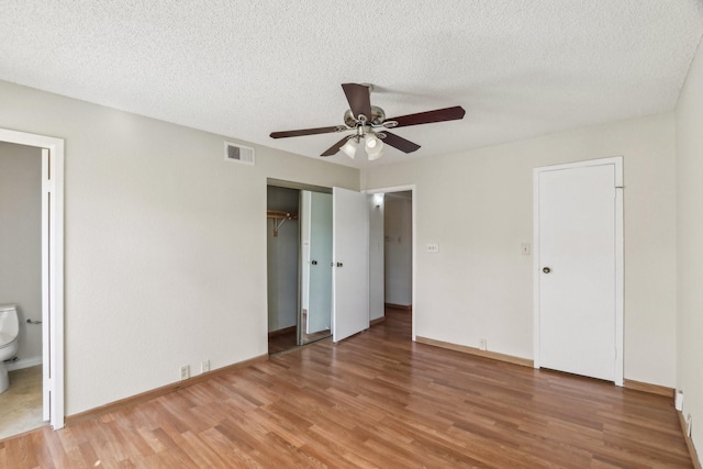 unfurnished bedroom featuring ensuite bathroom, ceiling fan, a textured ceiling, and wood-type flooring