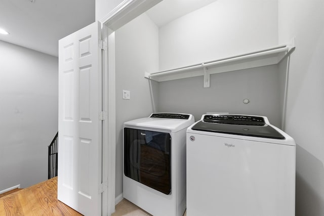 clothes washing area with washing machine and clothes dryer and light hardwood / wood-style flooring