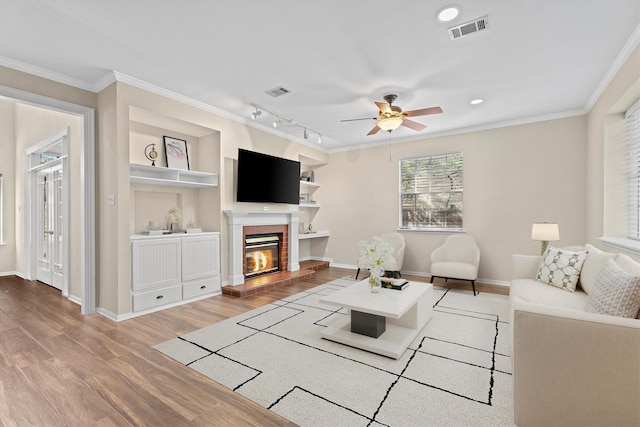 living room featuring crown molding, hardwood / wood-style floors, a fireplace, track lighting, and built in shelves