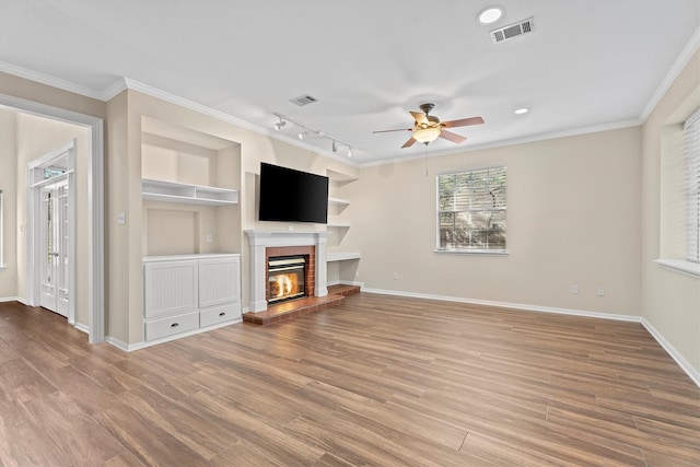 unfurnished living room featuring crown molding, light wood-type flooring, track lighting, ceiling fan, and a fireplace