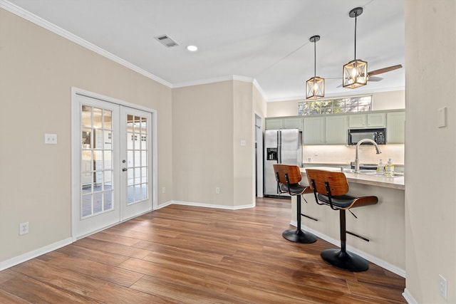 kitchen with a breakfast bar, green cabinets, french doors, stainless steel fridge with ice dispenser, and kitchen peninsula