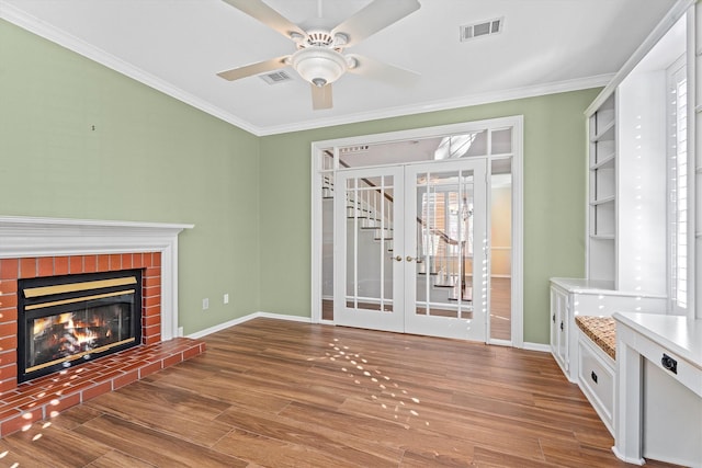 unfurnished living room with french doors, a brick fireplace, ornamental molding, hardwood / wood-style flooring, and ceiling fan