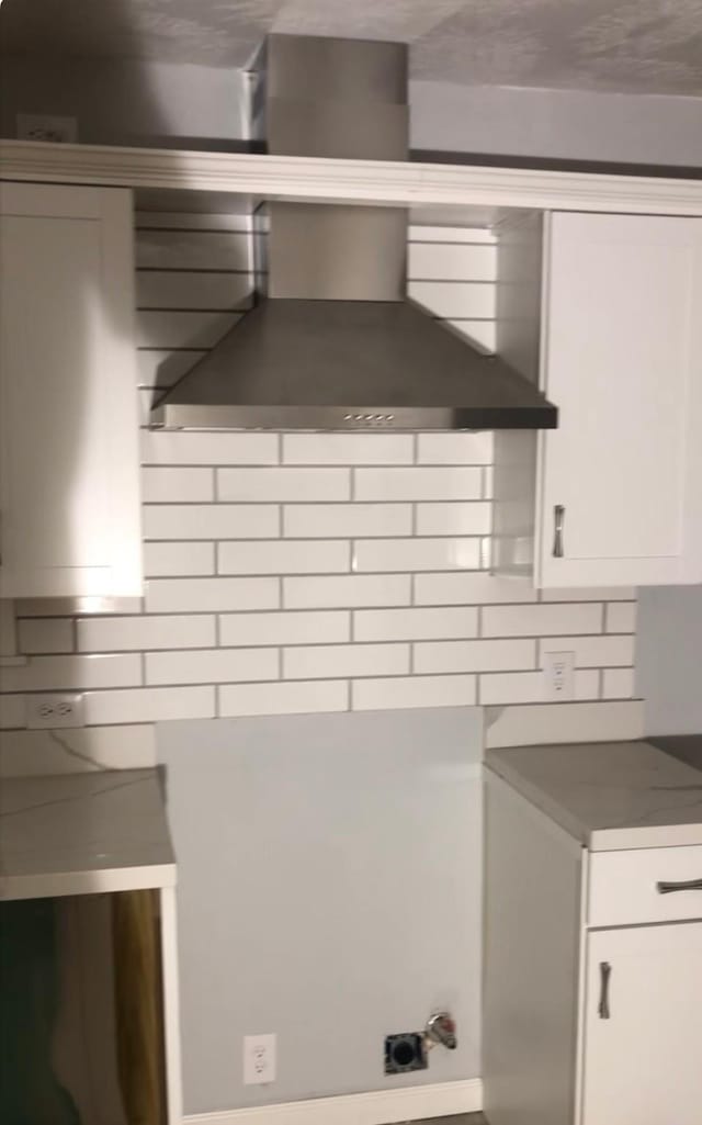 kitchen with wall chimney range hood and white cabinetry