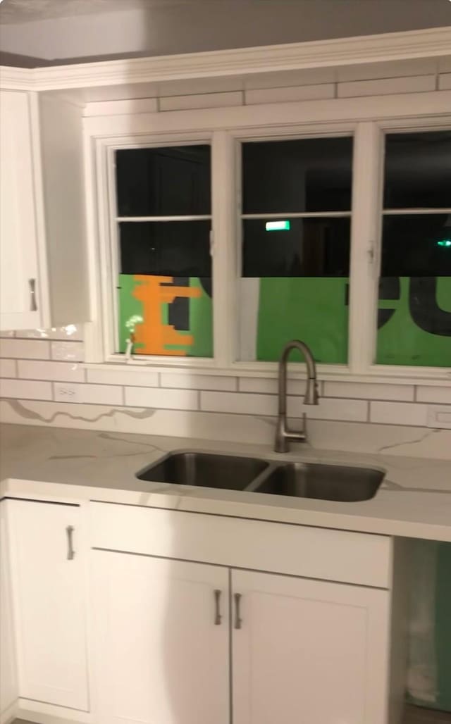 kitchen with light stone counters, sink, white cabinetry, and backsplash