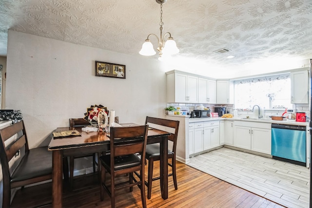 kitchen with dishwasher, white cabinets, pendant lighting, light hardwood / wood-style flooring, and sink