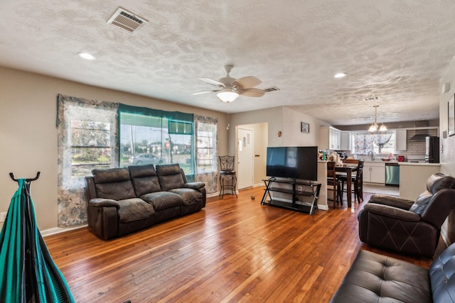 living room featuring wood-type flooring, sink, ceiling fan with notable chandelier, and a textured ceiling