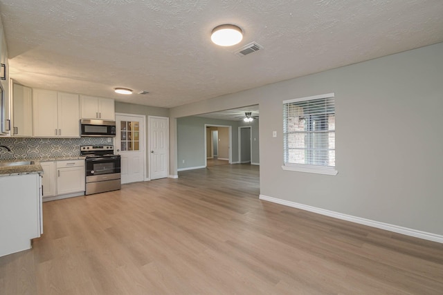 kitchen with light wood-type flooring, stainless steel appliances, backsplash, and white cabinetry