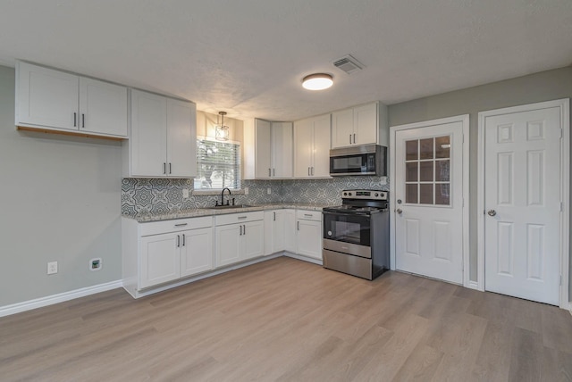 kitchen with white cabinetry, appliances with stainless steel finishes, light hardwood / wood-style flooring, light stone counters, and sink