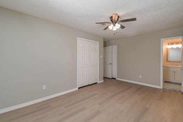 unfurnished bedroom with light wood-type flooring, ceiling fan, a textured ceiling, and ensuite bath