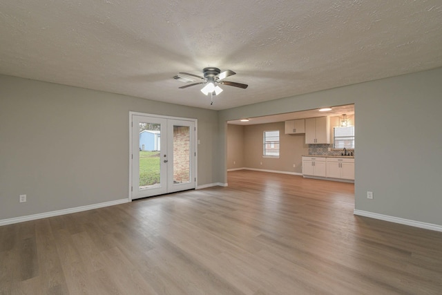 unfurnished living room with a textured ceiling, french doors, light hardwood / wood-style floors, sink, and ceiling fan