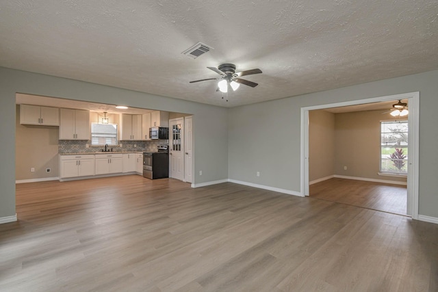 unfurnished living room with light hardwood / wood-style floors, sink, and a textured ceiling