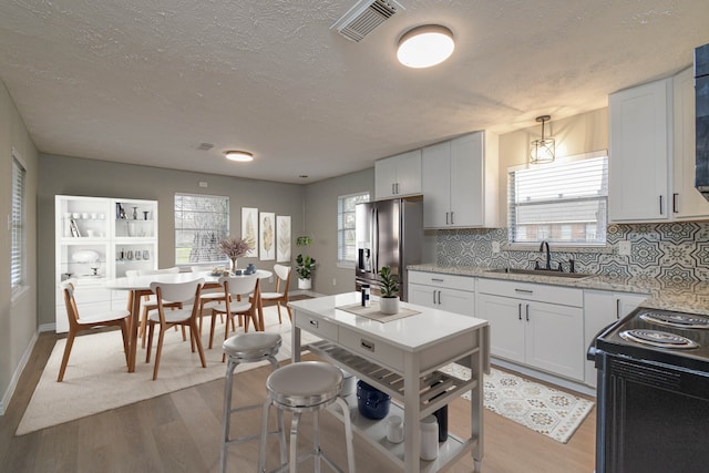 kitchen with white cabinetry, pendant lighting, stainless steel fridge, and sink