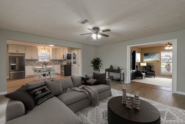 living room with ceiling fan, sink, a textured ceiling, and light wood-type flooring