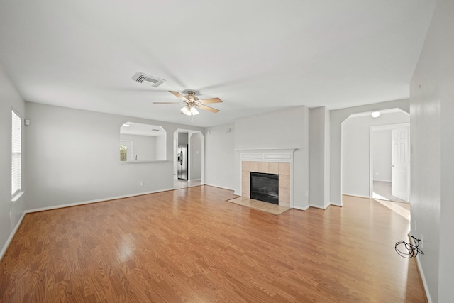 unfurnished living room featuring ceiling fan, light hardwood / wood-style floors, and a tiled fireplace