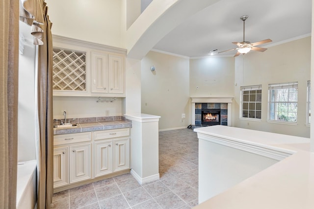 kitchen featuring ceiling fan, a tile fireplace, sink, crown molding, and cream cabinetry