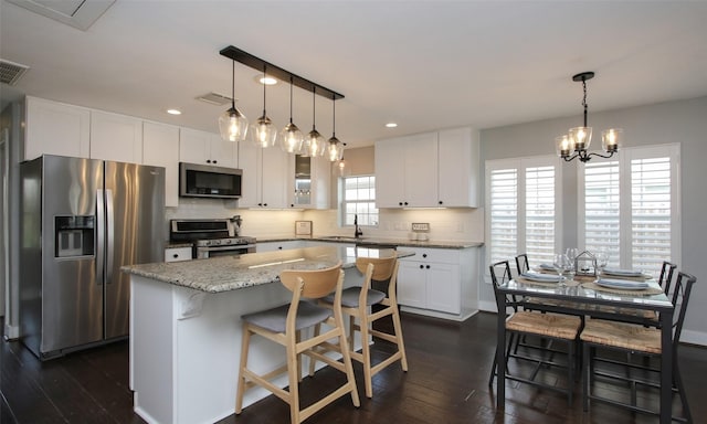 kitchen with hanging light fixtures, appliances with stainless steel finishes, white cabinetry, and a kitchen island