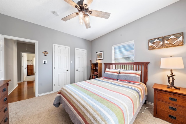 bedroom with ceiling fan, light colored carpet, and two closets