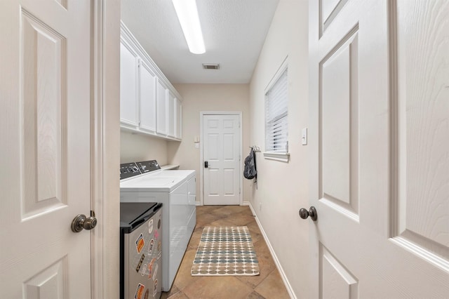 laundry room with light tile patterned floors, independent washer and dryer, a textured ceiling, and cabinets