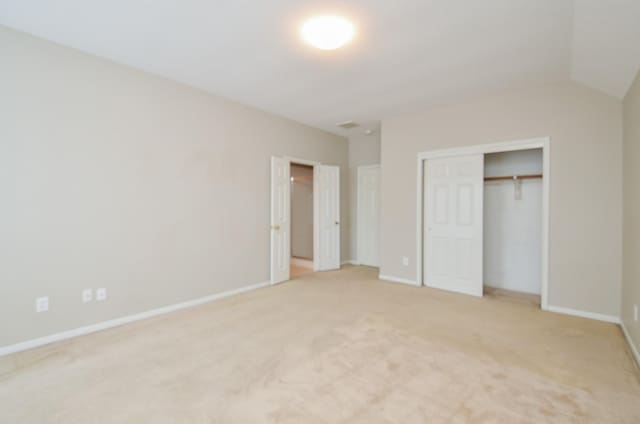 unfurnished bedroom featuring lofted ceiling, light carpet, and a closet