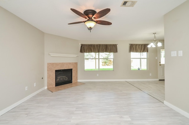 unfurnished living room featuring ceiling fan with notable chandelier, a fireplace, and light hardwood / wood-style flooring