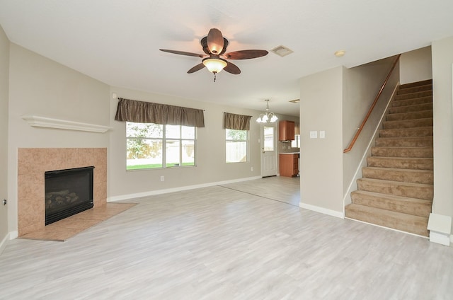 unfurnished living room with light hardwood / wood-style flooring, ceiling fan with notable chandelier, and a fireplace