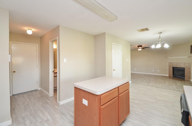 kitchen featuring hanging light fixtures, a center island, light hardwood / wood-style floors, a tiled fireplace, and ceiling fan with notable chandelier